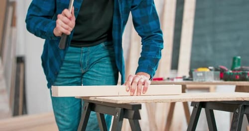 Close Up of Hammering a Nail Into Board A Carpenter Wearing a Red Flannel Shirt Jeans and Cloth