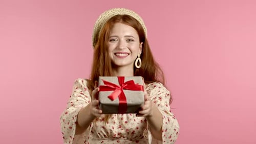 Smiling Woman Offers Gift on Pink Background