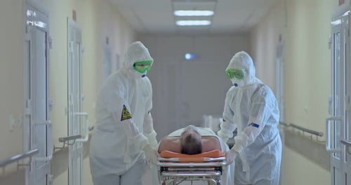 Doctors in Protective Suits Carry a Sick Patient on a Stretcher Along the Hospital Corridor