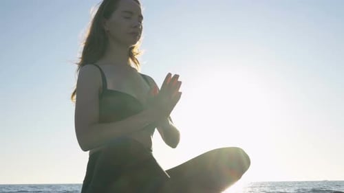 Young Caucasian Woman Practicing Yoga on the Beach Near Calm Sea