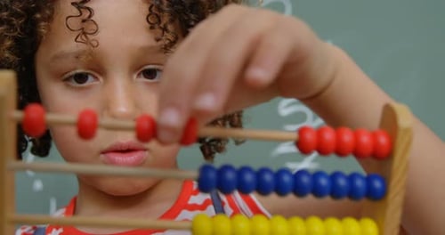 Vista frontal de una colegiala mestiza que aprende matemáticas con ábaco en un aula de la escuela 4k