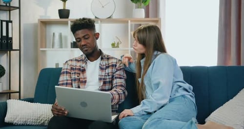 Amigos sentados juntos en el sofá de casa y hablando mientras ven el programa en la computadora