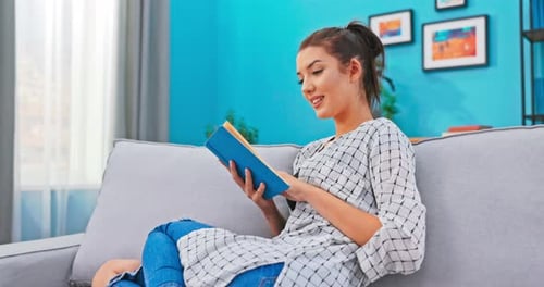 Beautiful Woman with Hair Pinned Up Relaxes in Homely Attire While Delving Into Book That