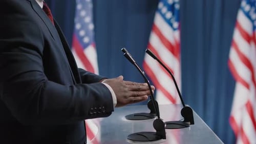 Adult Giving Speech at a Podium with Flags