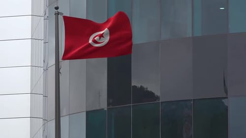 Waving Flag of Tunisia Against Modern Glass Building