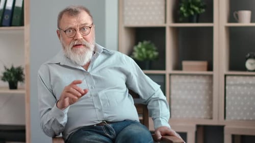 Man with Gray Beard Talks in Chair