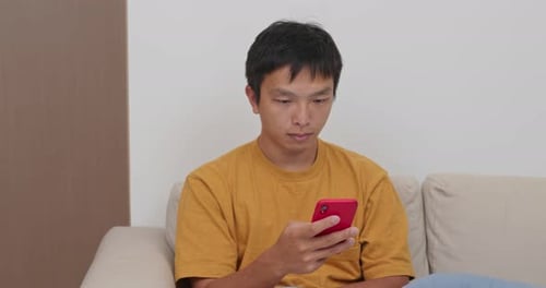 Young Adult Using Smartphone Sitting on Couch Indoors