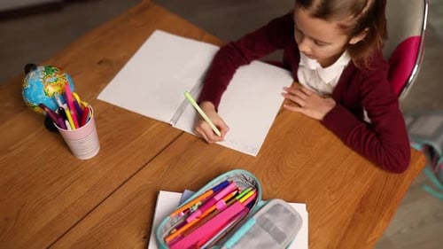 Child Writing in Notebook at Wooden Table