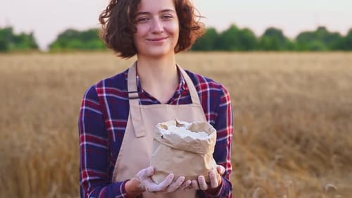 Joyful Smiling Woman With Flour. Woman With Hands Flour Holds Bag. Background Of Golden Wheat Field