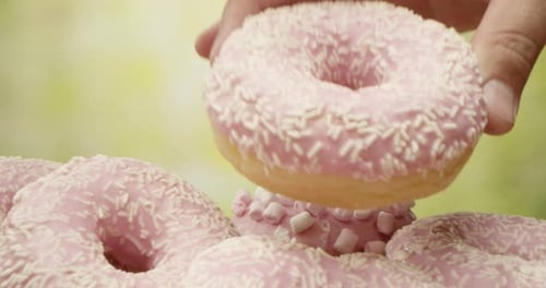 Palm Puts A Donut On A Pile Of Pink Donuts On The Table With Camera Dollying Out On Green Background