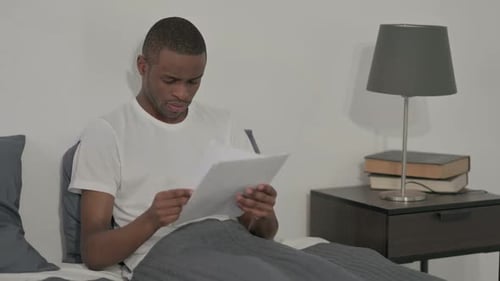 Man Reading Documents Reacts with Frustration in Bed