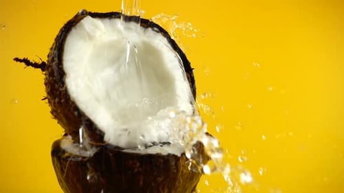 Water Pouring Into a Cracked Coconut Against Yellow