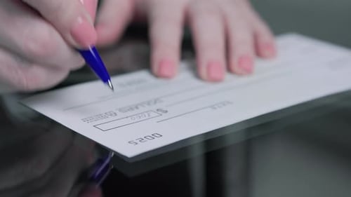 business woman hand signs and filling bank check for one thousand 1000 dollars