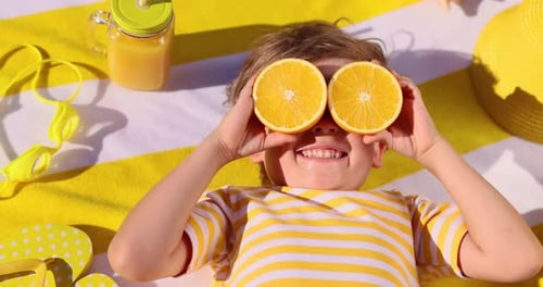 Smiling Child with Oranges on Summer Beach Towel