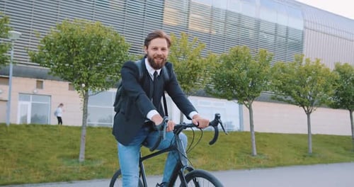 Hombre con ropa elegante sentado en su bicicleta y mirando a la cámara cerca de un gran edificio urbano moderno
