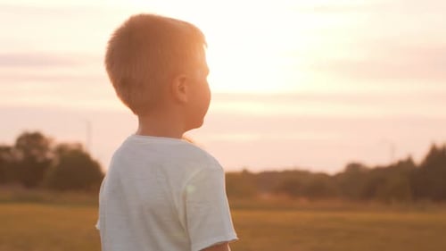 Kleiner Junge auf einem Feld bei Sonnenuntergang. Das Konzept von Kindheit, Freiheit und Inspiration.