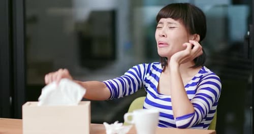 Woman Sits At Table Coughs And Blows Nose