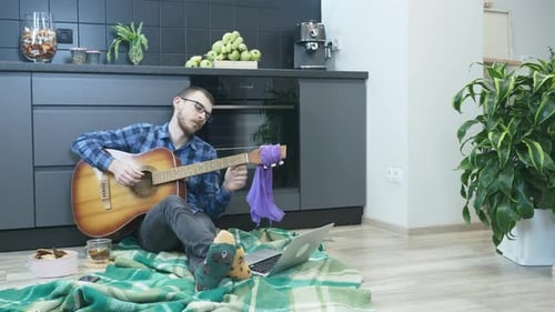 Homme assis sur le sol de la cuisine et accordant de la guitare. Processus de réglage de guitare
