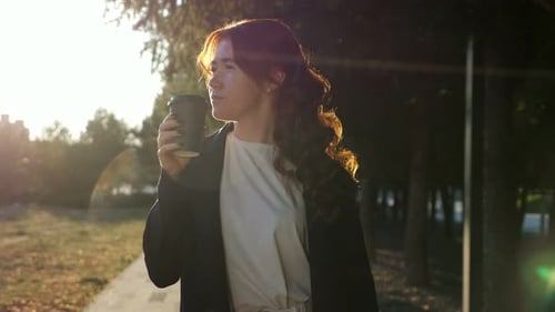 Confident Young Woman Drinks Coffee Walking Along Park Road