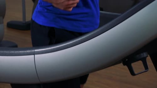 A Young Fit Man Jogs on a Treadmill in a Gym - Closeup