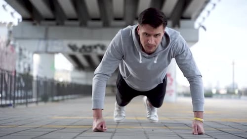 Sporty guy is doing push ups outdoors in evening in urban city.