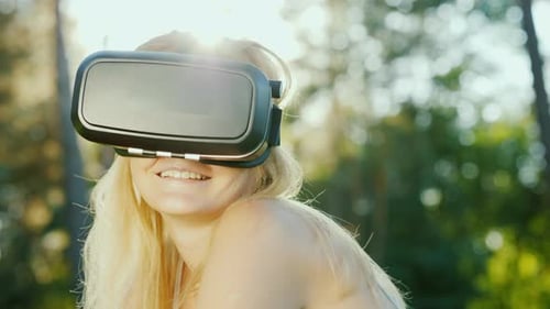 Attractive Woman in a Helmet of Virtual Reality. Sits in a Beautiful Place on the Nature
