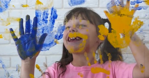 Smiling Child with Painted Handprints on Window