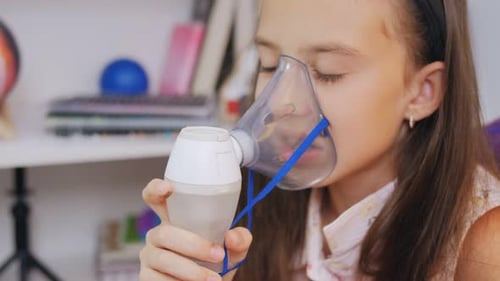 Niña inhala con un nebulizador médico mientras está sentada en la mesa
