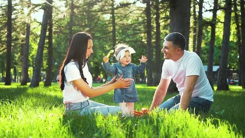 Happy Parents with Toddler Daughter Together on Green Grass in City Park