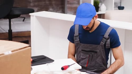 Close Up of Young Man in Coverall Using Laptop To Assembly Furniture