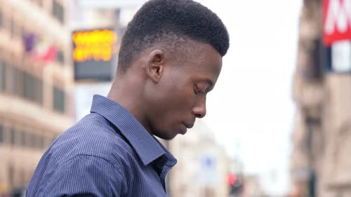 attractive young black man in the city, focused on typing on smart phone