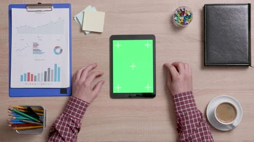 Top View of Male Hands Scrolling on the Right Edge of a Green Screen on a Black Tablet