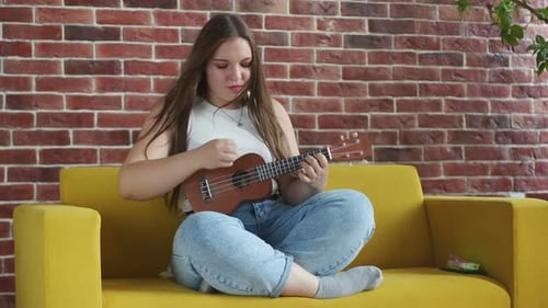 Woman Plays Ukulele on Yellow Couch Indoors