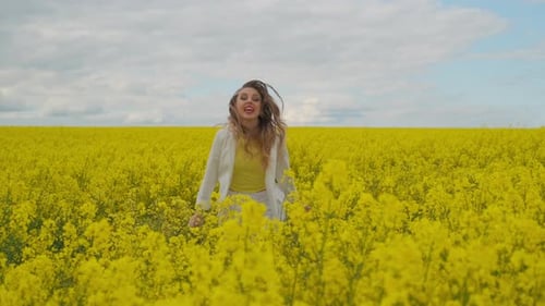 An Energetic Jumping and Dancing Female Singer with a Microphone in a Field of Rapeseed with Yellow