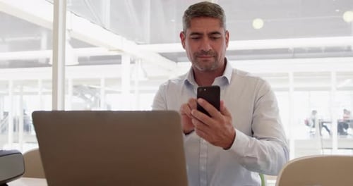 Man Using Smartphone at Desk with Laptop