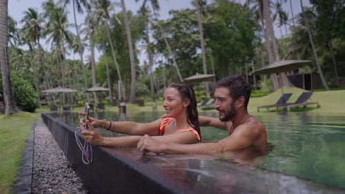 A Side View of a Happy Young Couple Taking Selfie Photo at Edge of Swimming Pool