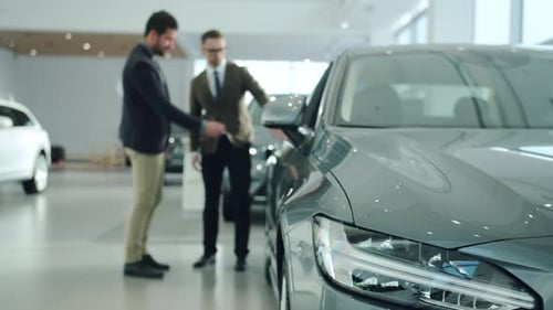 Handsome Guy Talking To Sales Agent in Car Dealership, Focus on Expensive Automobile. Focus on Car