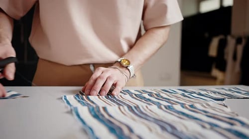 Person Cutting Striped Fabric with Scissors on Table