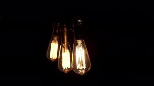 Retro Light Bulb on Black Background. Three Vintage Lights Swing in the Dark on Wire. Yellow Light