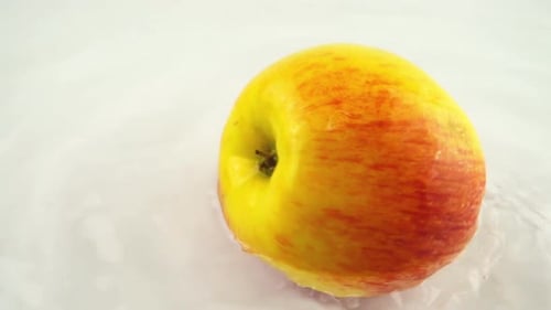 Pomme mûre en rotation dans l'eau sur fond blanc. Ralenti.