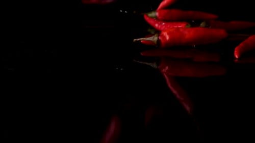 Red Chili Peppers Falling on Black Reflective Surface