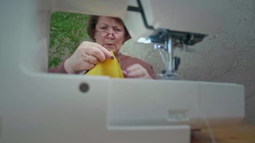 Woman Using Sewing Machine To Sew Yellow Fabric