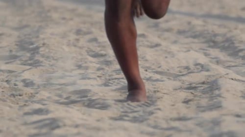A young mans barefoot feet running on the beach.