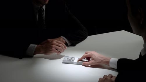 Businessman giving bribe money to his partner in dark room after making a deal