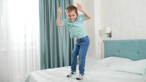 Slow Motion of Happy Laughing Boy Jumping and Dancing on Big Bed in Bedroom with Big Window