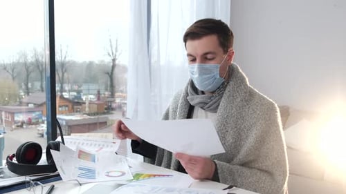 Man with Mask Reviews Financial Documents at Home