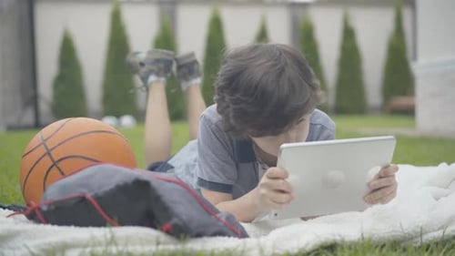 Wide Shot Portrait of Happy Relaxed Caucasian Boy Gaming Online Using Tablet. Cheerful Kid Enjoying