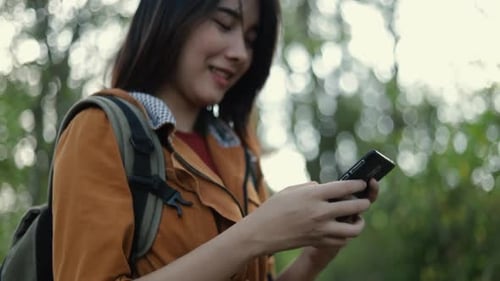 Smiling young Asian girl tourists using smartphones in the forest on sunny beautiful summer.