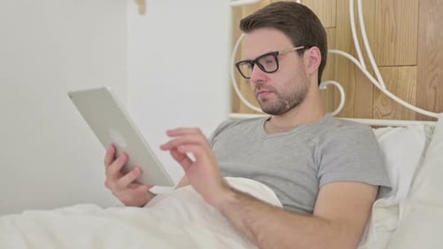 Man Using Tablet Device While Sitting in Bed