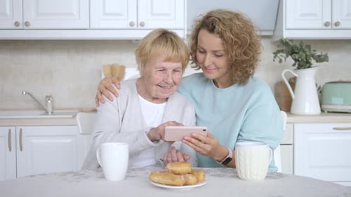 Woman Embraces Senior Woman Looking at Mobile Phone
